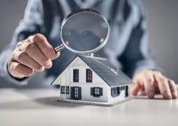 Your property inspection check list. Man holding a magnifying glass over a model house inspecting the detail.
