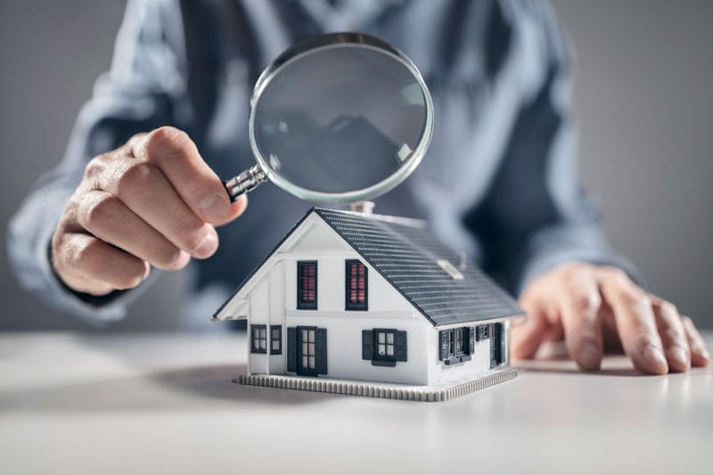 Your property inspection check list. Man holding a magnifying glass over a model house inspecting the detail.